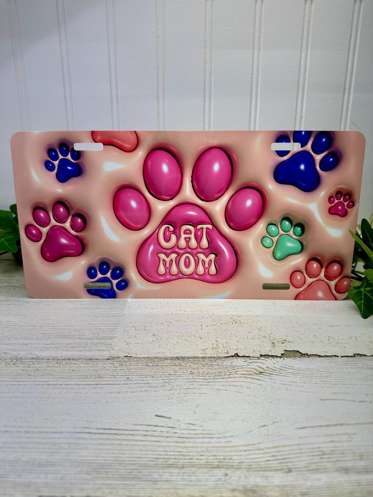 A 3D inflated-style aluminum license plate with a design that includes paw prints and the text 'Cat Mom'.